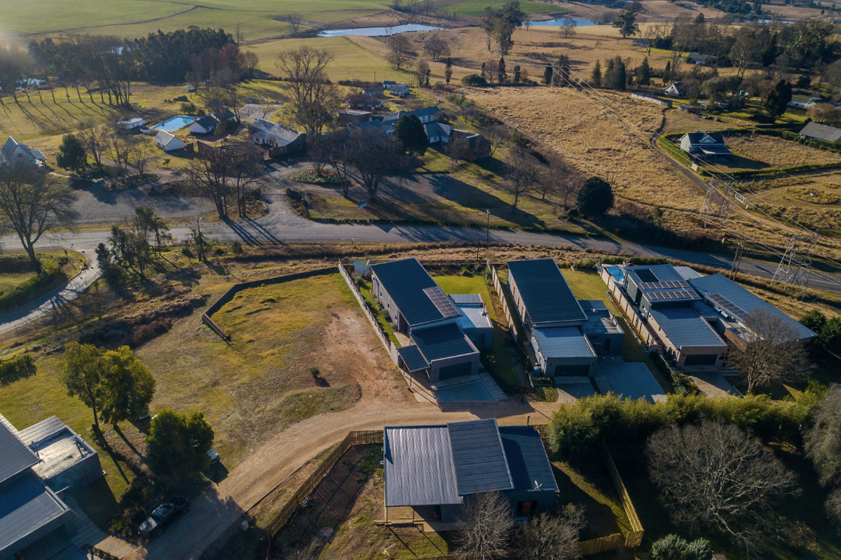 Aerial view of a residential development featuring modern homes with metal roofs and solar panels, set within a rural landscape.