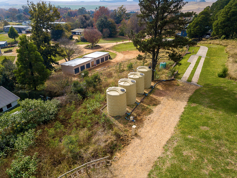 Aerial view of a residential plot featuring a row of water storage tanks, a pump system, and a gravel driveway leading to an outbuilding.