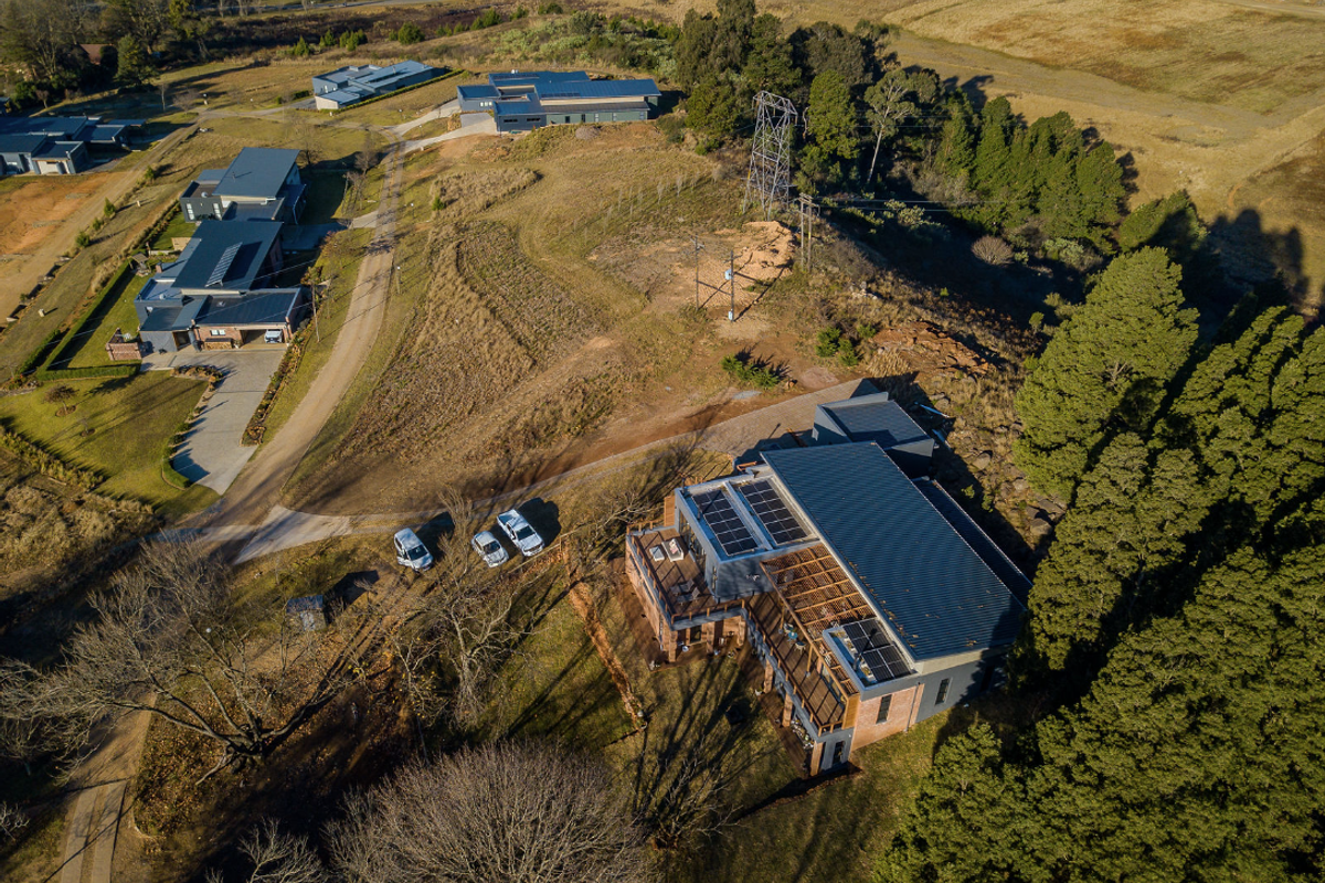 Aerial view of a residential property featuring a modern home with solar panels, expansive decking, and surrounding rural landscape.