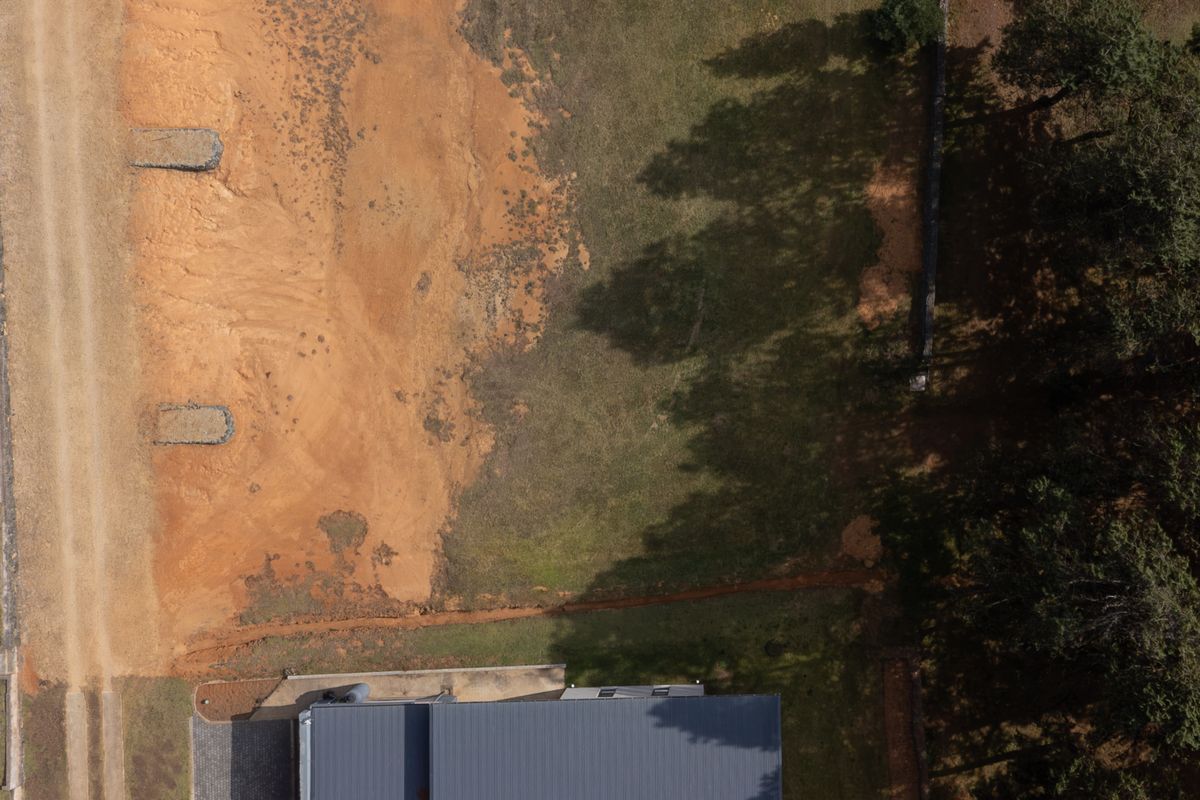 Aerial view of a vacant residential plot featuring a dirt access path, natural vegetation, and mature trees along the boundary.