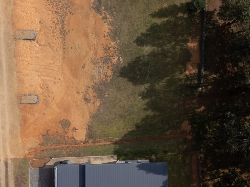 Aerial view of a vacant residential plot featuring a dirt access path, natural vegetation, and mature trees along the boundary.