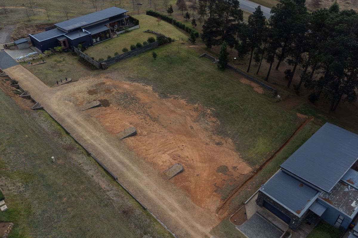 Aerial view of a vacant residential plot featuring cleared land, established retaining walls, and gravel driveway access situated between existing modern homes.