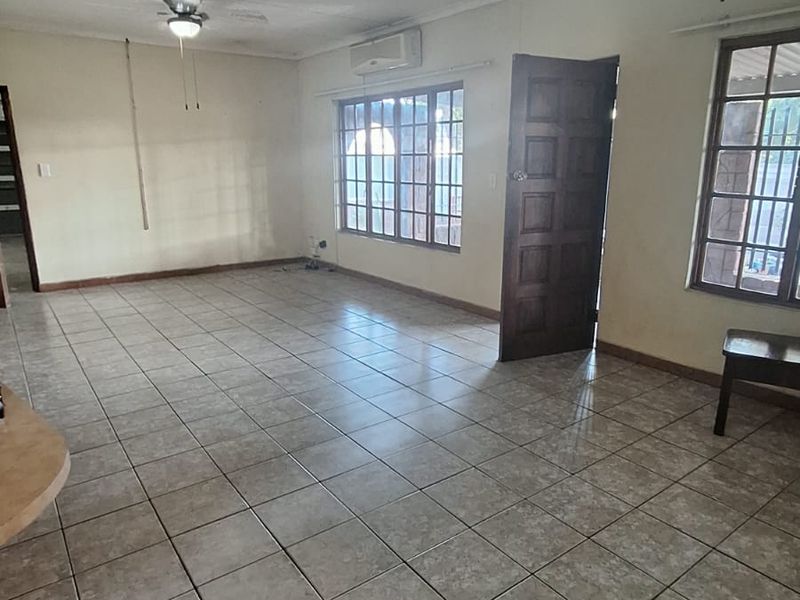 Spacious, light-filled living area featuring neutral tiled flooring, ceiling fans, and a wall-mounted air conditioning unit, offering a versatile blank canvas.
