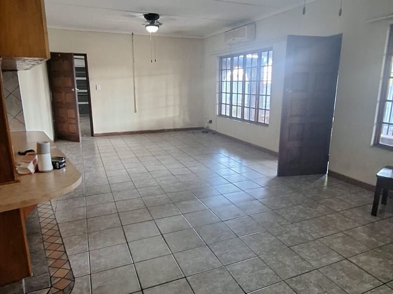 Spacious open-plan living area featuring tiled flooring, ceiling fans, and a split-system air conditioner, offering a blank canvas for renovation.