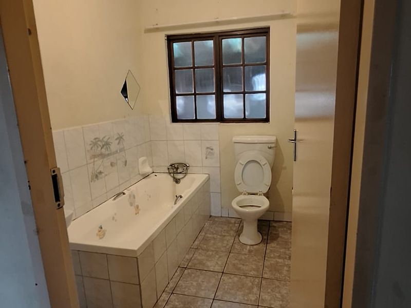 A dated bathroom featuring a built-in bathtub, ceramic tiling, and a standard toilet, requiring cosmetic updates to modernize the space.