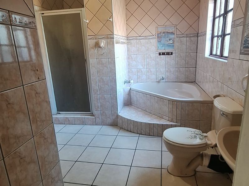 A dated bathroom featuring a corner bathtub, separate shower enclosure, toilet, and pedestal basin with neutral ceramic tiling throughout.