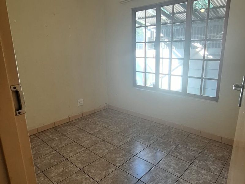 An empty bedroom featuring tiled flooring, a ceiling fan, and a window with security bars, offering a blank canvas for potential updates.