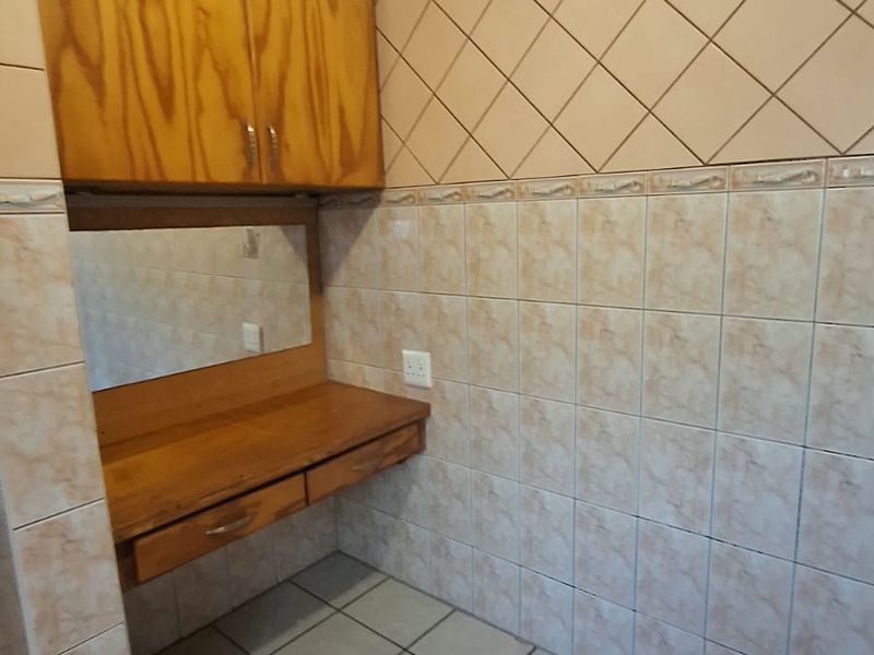A functional kitchen area featuring built-in wooden cabinetry, a desk space, and full-height ceramic wall tiling.