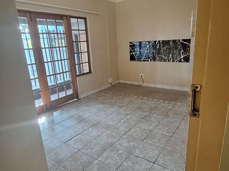 An empty living room featuring tiled flooring, a ceiling fan, and a wooden framed glass door leading to the exterior.