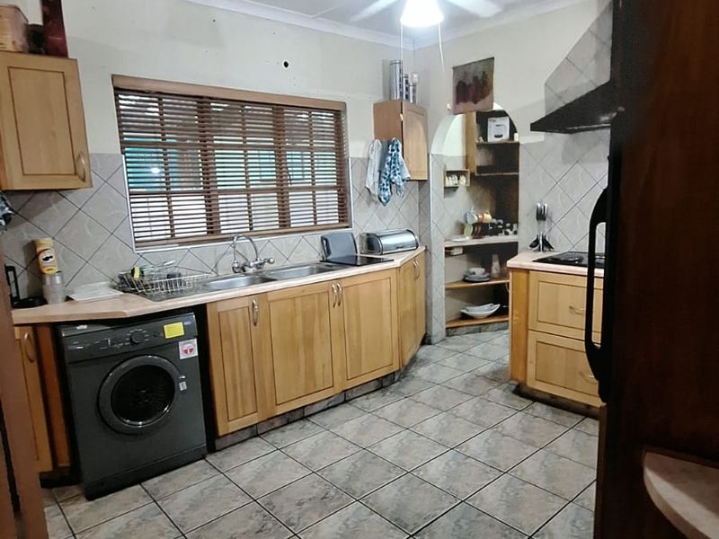 A dated kitchen featuring wooden cabinetry, tiled flooring, and a separate scullery area, requiring cosmetic updates and ceiling repairs.