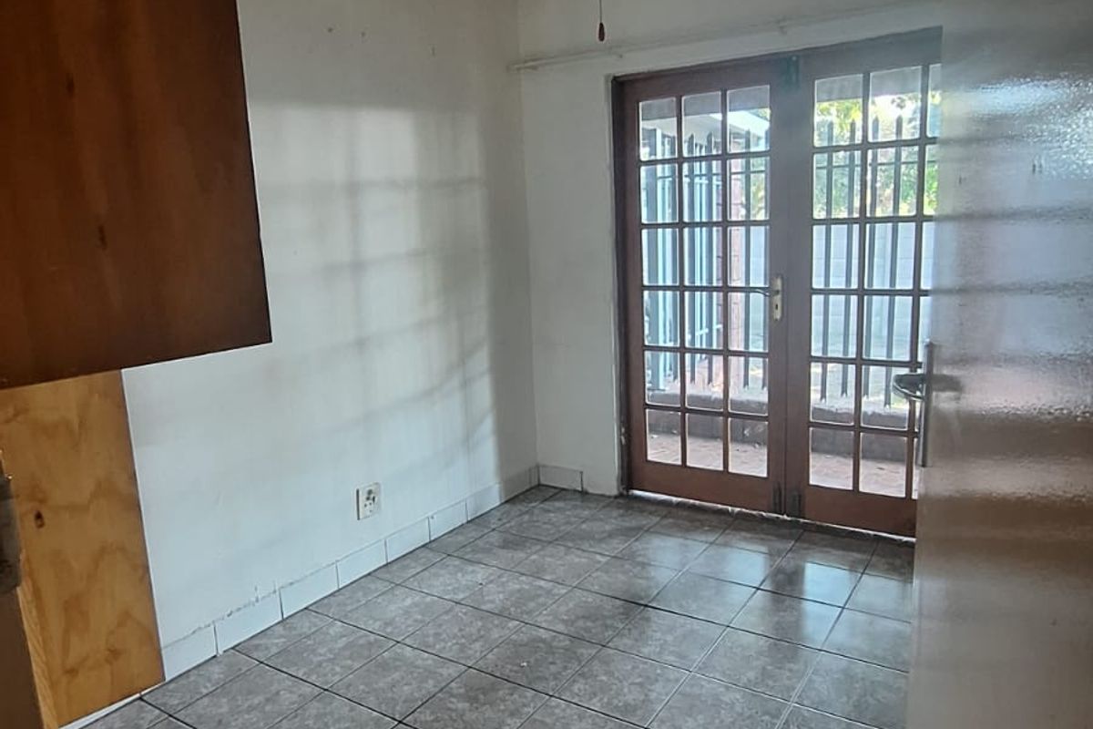 An empty living area featuring tiled flooring, a ceiling fan, and wooden french doors leading to an outdoor space.