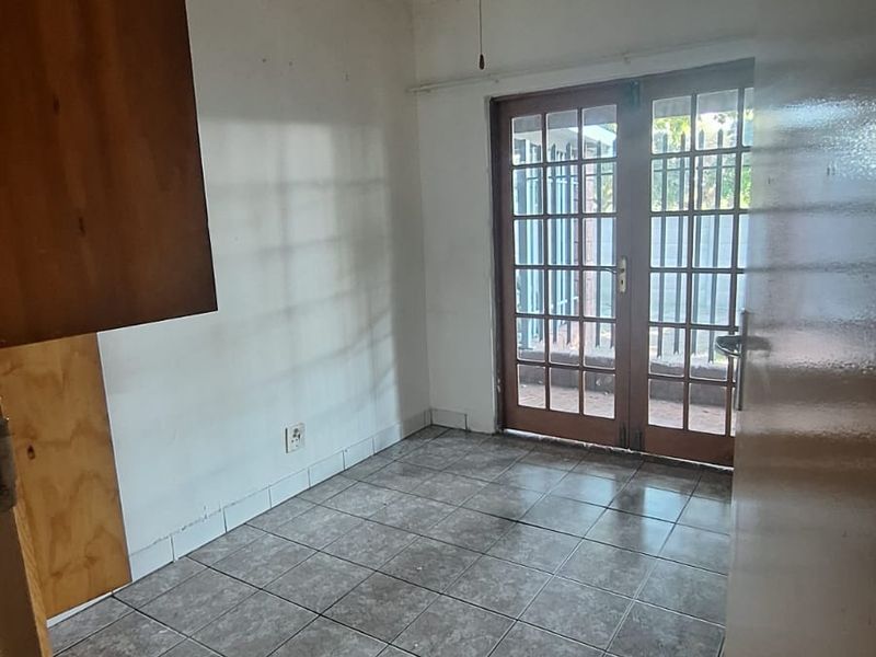An empty living area featuring tiled flooring, a ceiling fan, and wooden french doors leading to an outdoor space.