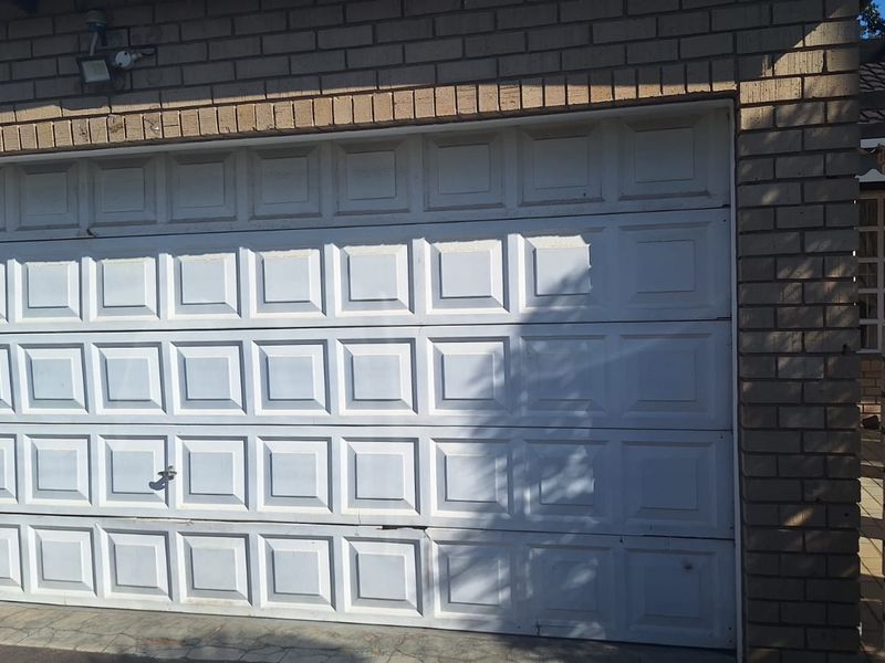 Exterior view of a brick townhouse garage featuring a white sectional door and an integrated security floodlight.