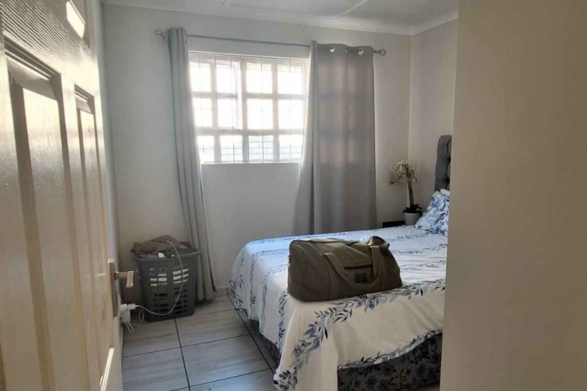 A functional bedroom featuring light-toned tiled flooring, a window with security bars, and a simple ceiling light fixture.