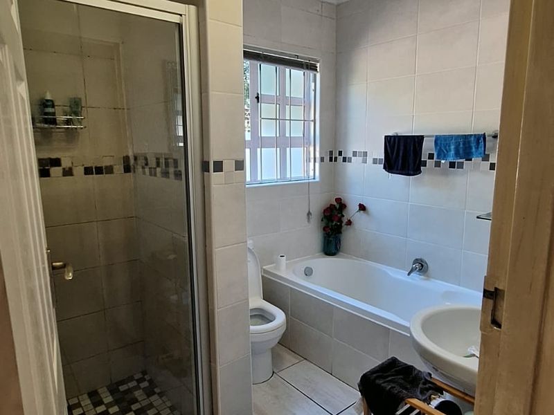 A functional bathroom featuring a separate shower, bathtub, toilet, and pedestal basin, with tiled finishes and visible ceiling maintenance required.