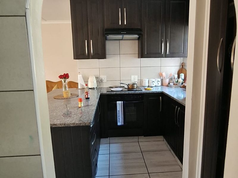 A functional kitchen featuring dark wood cabinetry, granite countertops, a built-in oven with extractor fan, and neutral ceramic floor tiling.