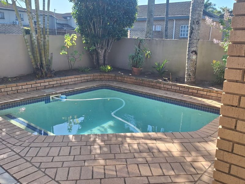 A private outdoor pool area featuring brick paving, a surrounding boundary wall, and established garden landscaping.