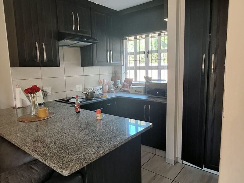 Compact kitchen featuring dark wood cabinetry, granite countertops, a breakfast bar, and tiled flooring, offering a functional layout for daily meal preparation.