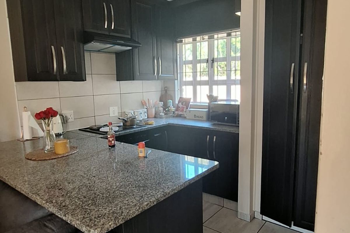 Compact kitchen featuring dark wood cabinetry, granite countertops, a breakfast bar, and tiled flooring, offering a functional layout for daily meal preparation.