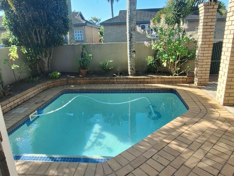 A private outdoor swimming pool area featuring brick paving, a brick pillar, and established garden landscaping within a secure boundary wall.