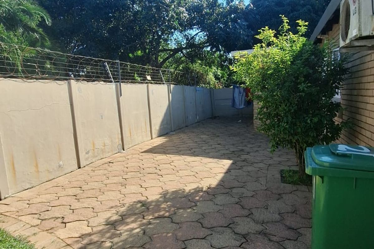 A paved rear courtyard area featuring a perimeter wall with electric fencing and an external air conditioning unit.