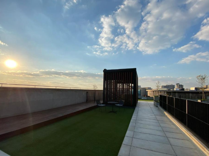 Spacious rooftop terrace featuring timber decking, artificial lawn, and a modern pergola structure with panoramic city views.
