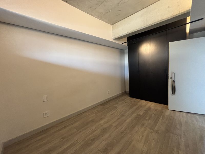 A modern, empty bedroom featuring sleek built-in cupboards, exposed concrete ceiling details, and contemporary laminate flooring.
