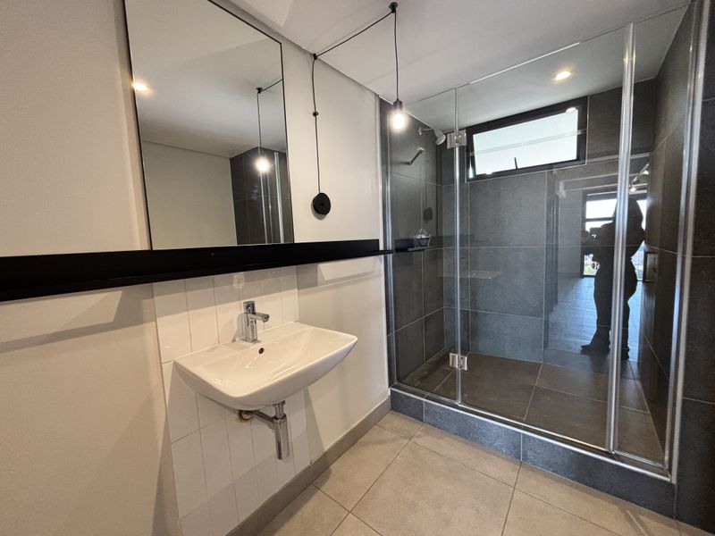 Modern bathroom featuring a wall-mounted basin, chrome fixtures, and a spacious glass-enclosed shower with dark tiled finishes.