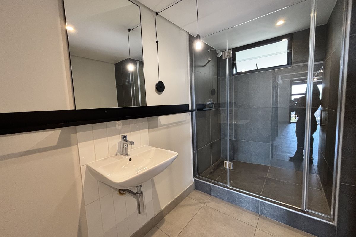 Modern bathroom featuring a wall-mounted basin, chrome fixtures, and a spacious glass-enclosed shower with dark tiled finishes.