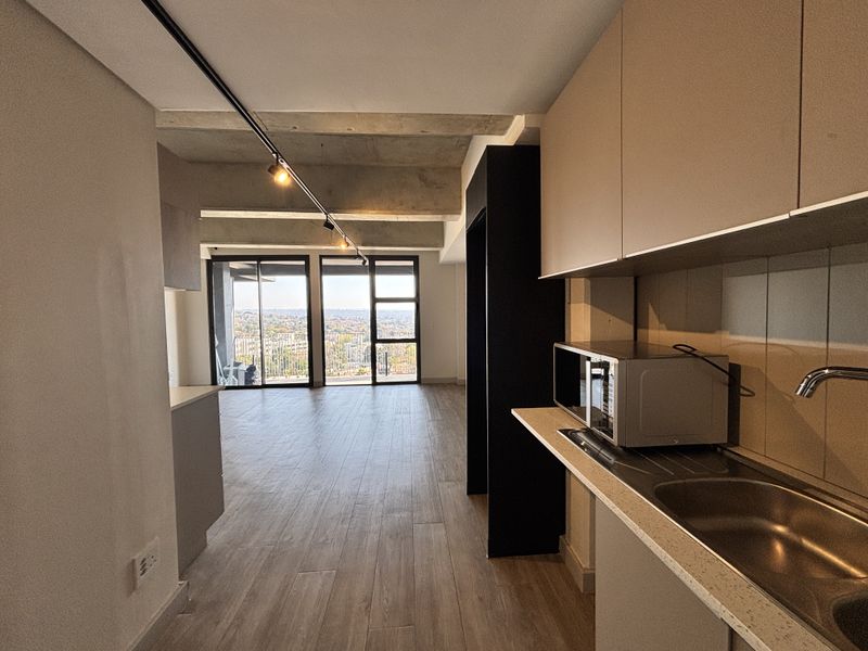 Modern open-plan apartment featuring an exposed concrete ceiling, sleek cabinetry, and large sliding doors leading to a balcony with expansive city views.