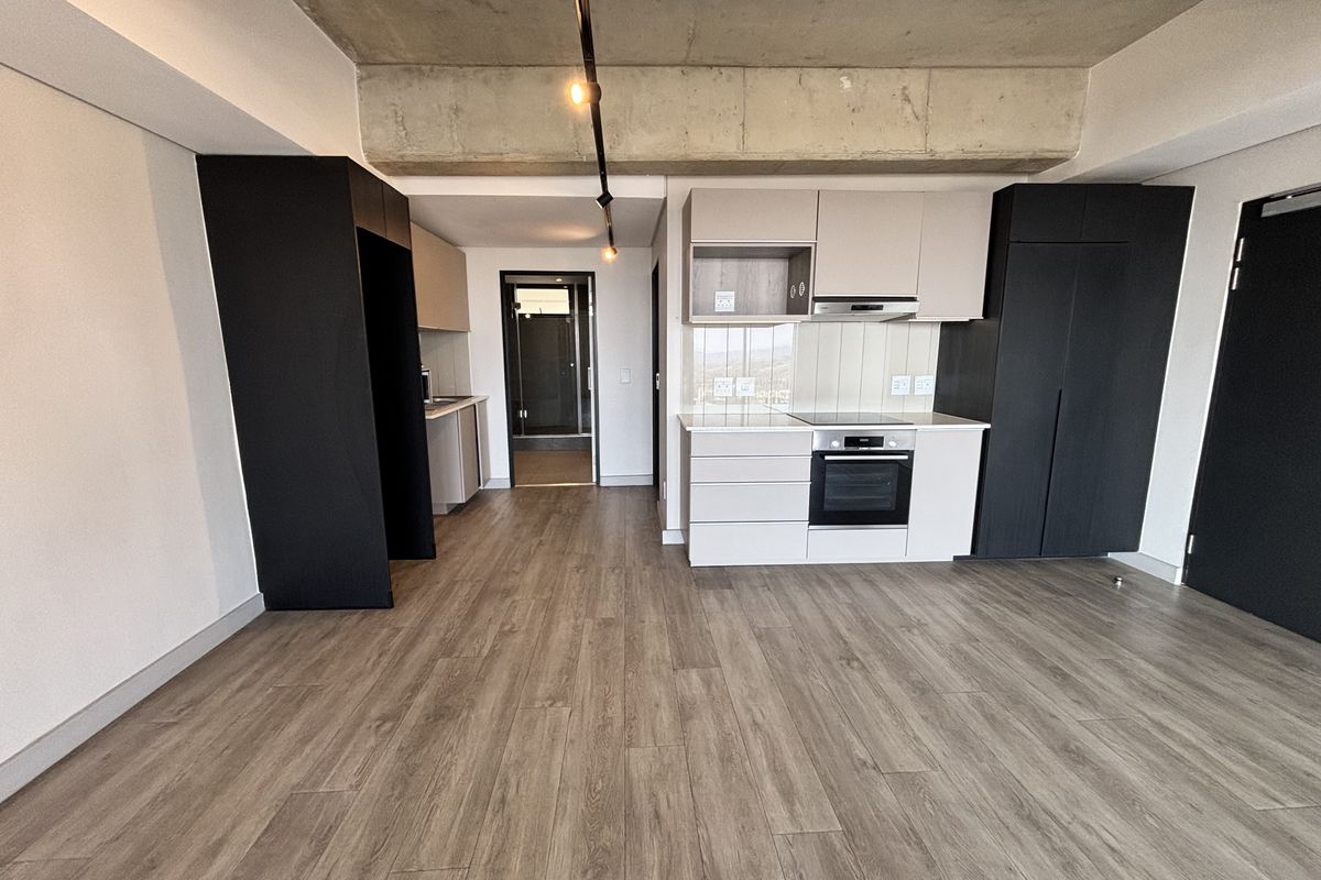 Modern open-plan kitchen featuring sleek built-in cabinetry, integrated appliances, and an exposed concrete ceiling, set against durable laminate flooring in a contemporary apartment.