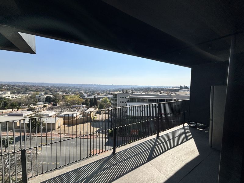 A spacious covered balcony featuring modern tiled flooring and a metal balustrade, offering expansive elevated views of the surrounding urban landscape.