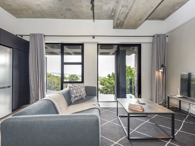 Modern open-plan living area featuring an exposed concrete ceiling, sleek built-in cabinetry, and large sliding glass doors leading to a private balcony.