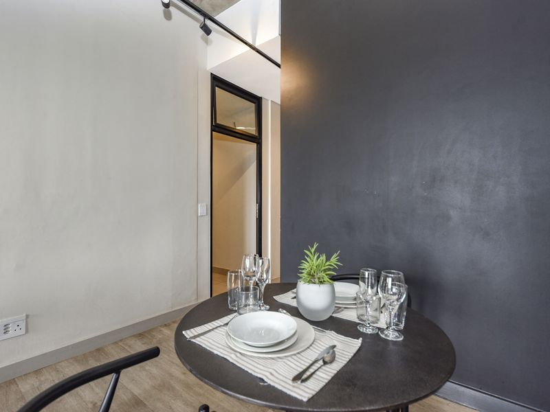 A modern dining area featuring a striking black feature wall, track lighting, and durable laminate flooring, leading into an adjacent room.