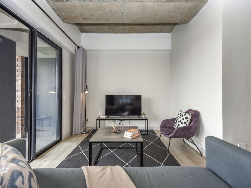 Modern living room featuring an exposed concrete ceiling, laminate flooring, and large sliding glass doors providing access to the outdoor area.