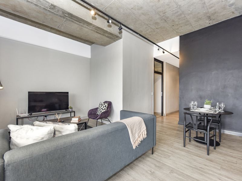 Modern open-plan living and dining area featuring an exposed concrete ceiling, track lighting, and contemporary laminate flooring.