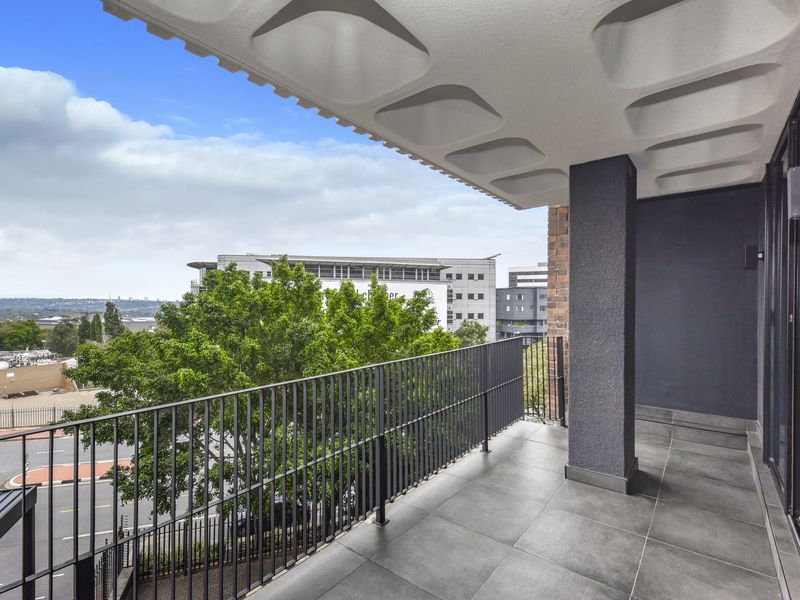 A modern, covered balcony featuring sleek tiled flooring, a sturdy metal balustrade, and an elevated view of the surrounding urban landscape.