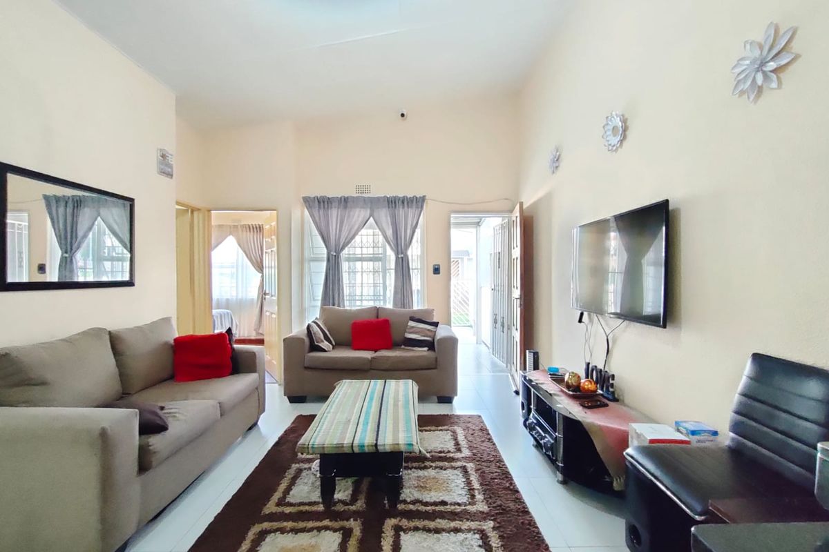 A well-lit living room featuring tiled flooring, neutral wall finishes, and direct access to an adjacent room and exterior area via a security gate.