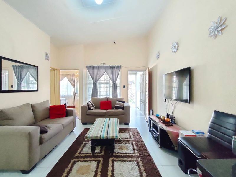 A well-lit living room featuring tiled flooring, neutral wall finishes, and direct access to an adjacent room and exterior area via a security gate.