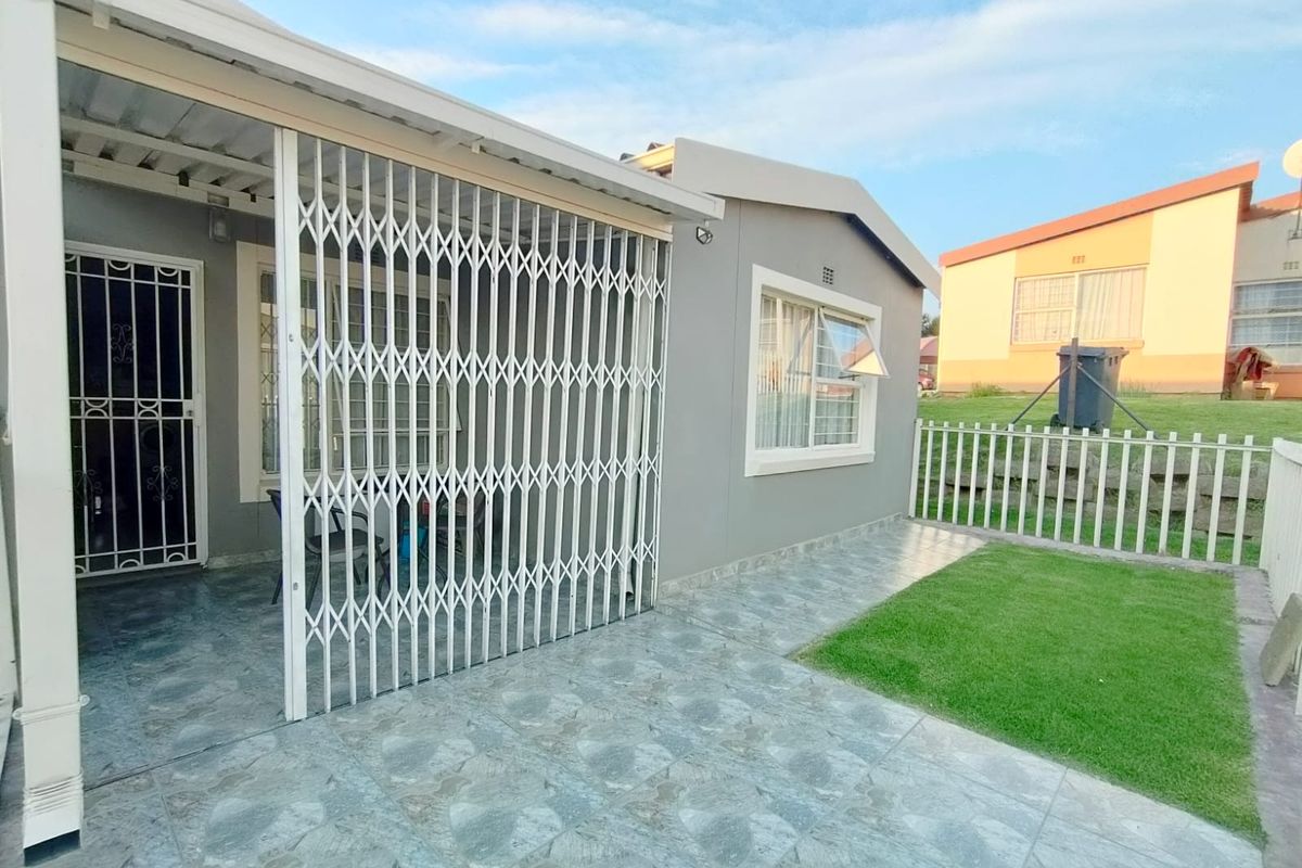 A rear exterior view of the townhouse featuring a tiled patio area, security gates, and a small private lawn with perimeter fencing.