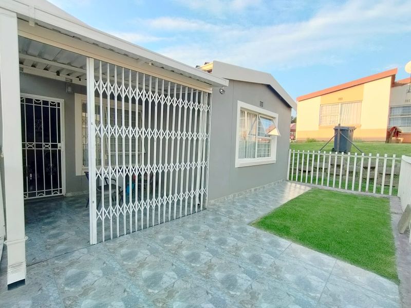 A rear exterior view of the townhouse featuring a tiled patio area, security gates, and a small private lawn with perimeter fencing.