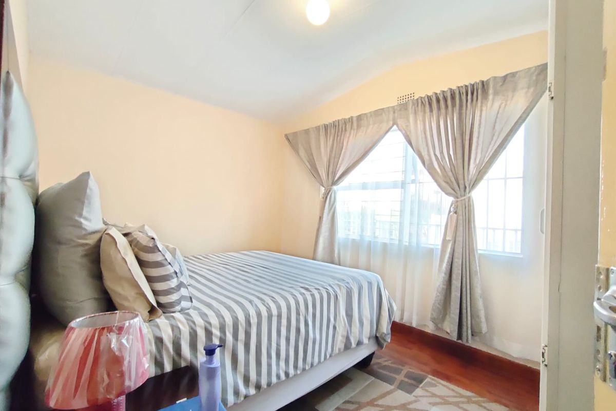 A standard bedroom featuring timber flooring and a window fitted with security bars, providing natural light.