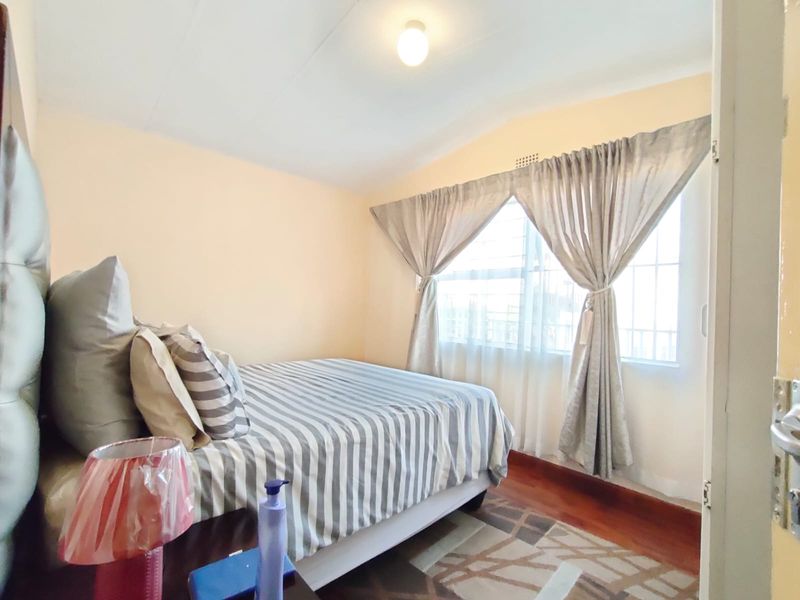 A standard bedroom featuring timber flooring and a window fitted with security bars, providing natural light.