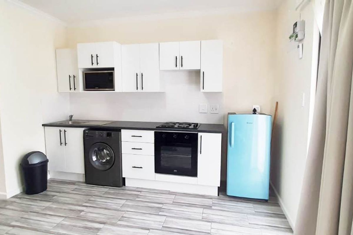 A compact kitchen featuring white cabinetry, dark countertops, built-in oven, gas hob, and integrated microwave, with a view into the adjacent bathroom.