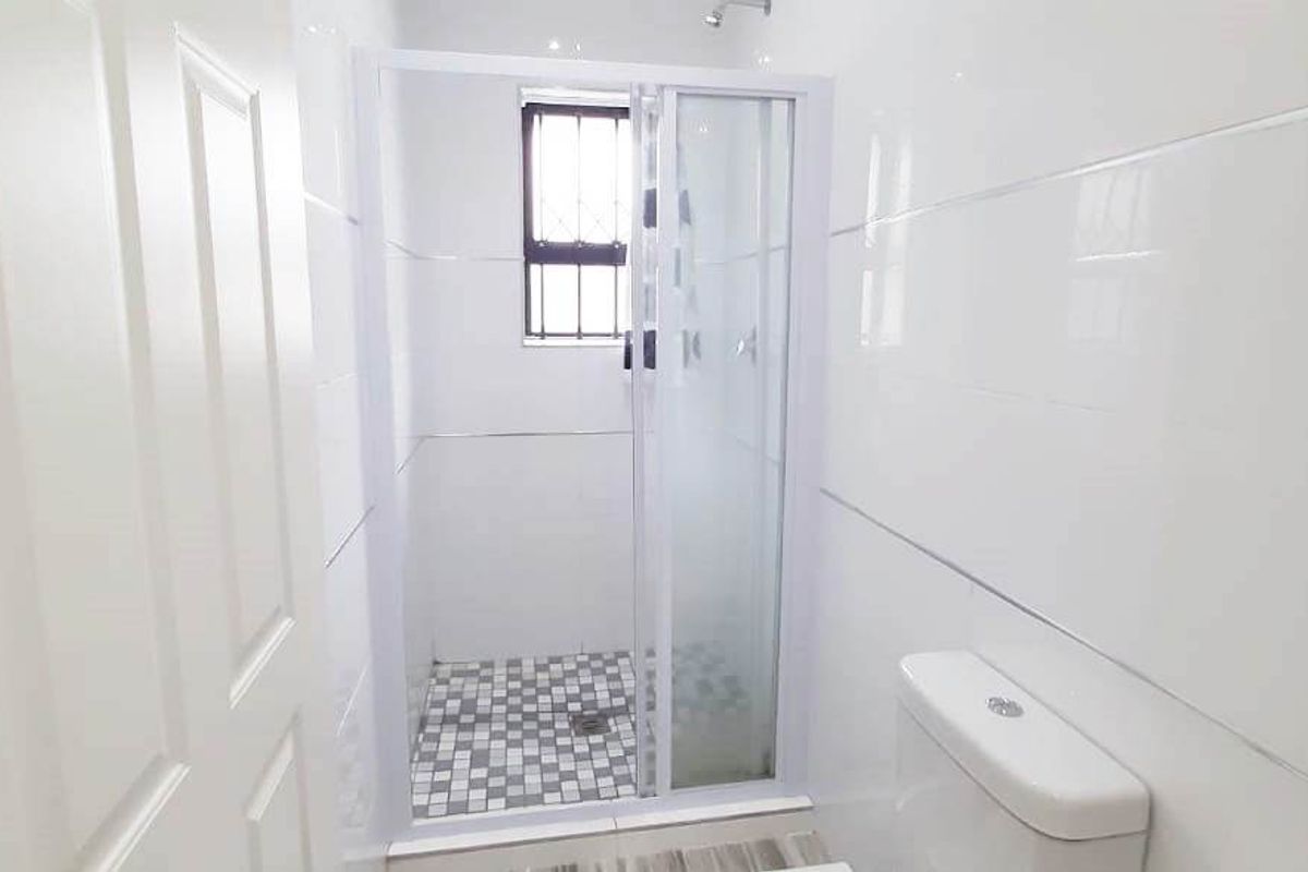 A clean, functional bathroom featuring a shower enclosure with mosaic floor tiling, white wall tiles, and a standard toilet.