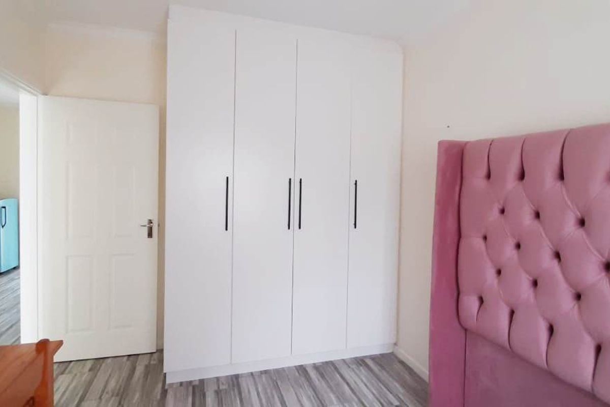 A well-maintained bedroom featuring modern white built-in wardrobes and durable laminate flooring, offering a clean and functional living space.