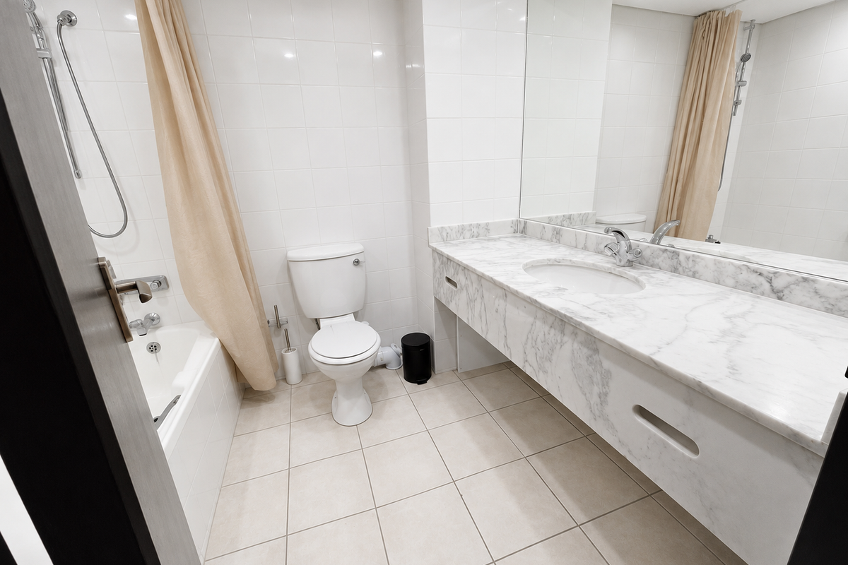 A clean, functional bathroom featuring a marble vanity countertop, undermount sink, large wall mirror, and a combined bathtub and shower area with white tiling.