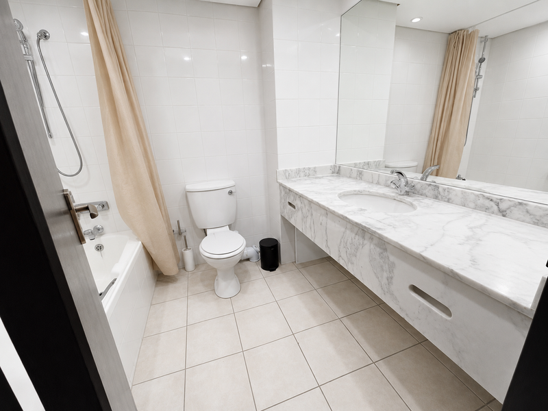 A clean, functional bathroom featuring a marble vanity countertop, undermount sink, large wall mirror, and a combined bathtub and shower area with white tiling.