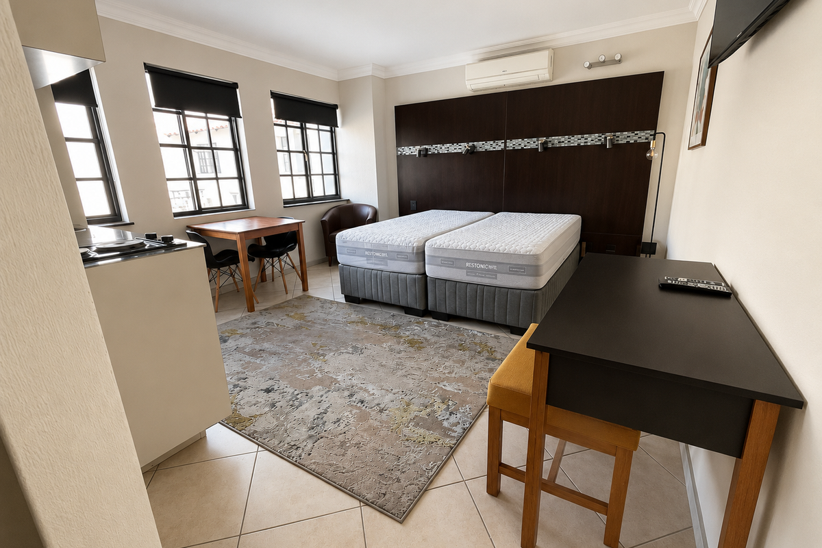 An open-plan studio apartment featuring a kitchenette, tiled flooring, air conditioning, and a built-in headboard wall unit.