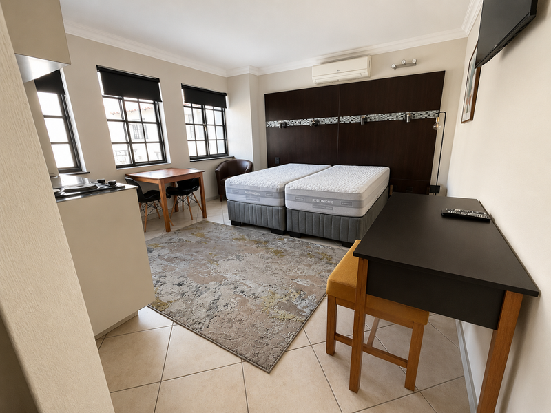 An open-plan studio apartment featuring a kitchenette, tiled flooring, air conditioning, and a built-in headboard wall unit.